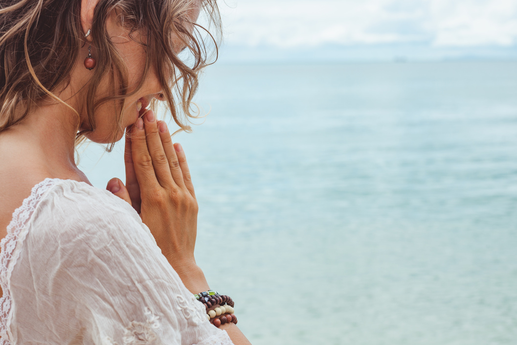 Beautiful young woman praying on the beach